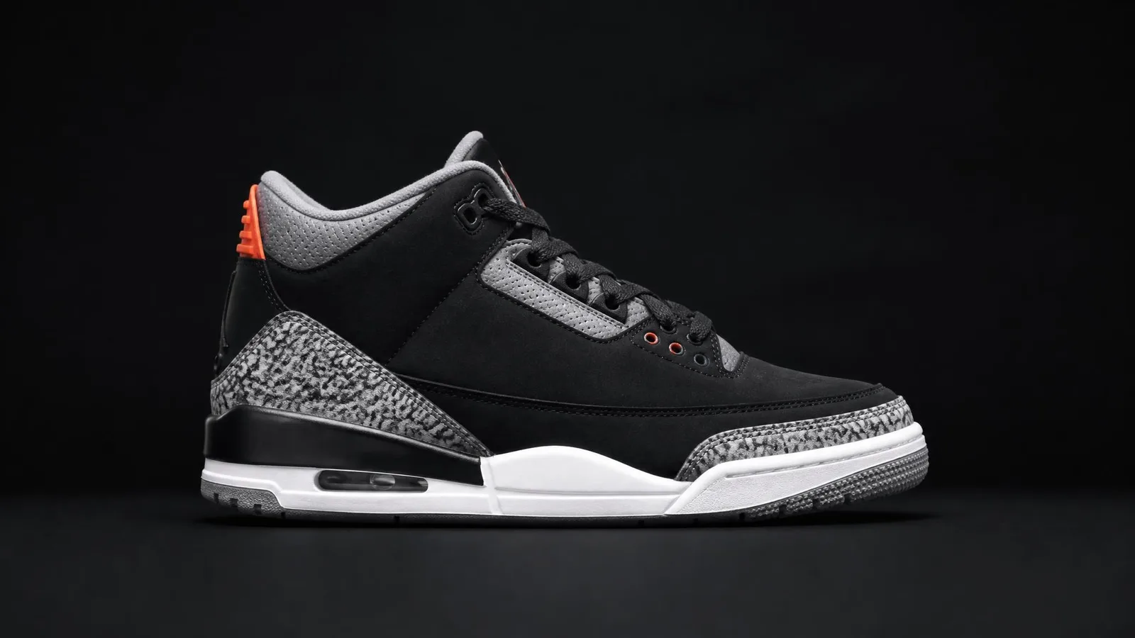 A single sneaker photographed in precise side profile against a dark background with a warm accent-colored heel tab, representing a catalogued pair with tracked rack value data