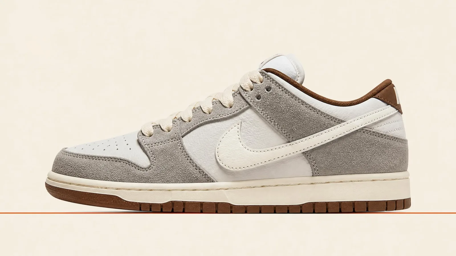 A Nike SB Dunk photographed in clean full-length side profile against a warm cream background with a thin orange baseline beneath the sole, shot in even studio lighting with no shadows.