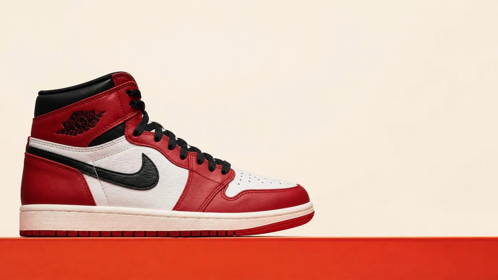 A deadstock pair of Air Jordan 1s shot in clean side-profile silhouette against a warm cream background, lit evenly with a subtle orange accent beneath the sole — collector-catalogue style product photography.