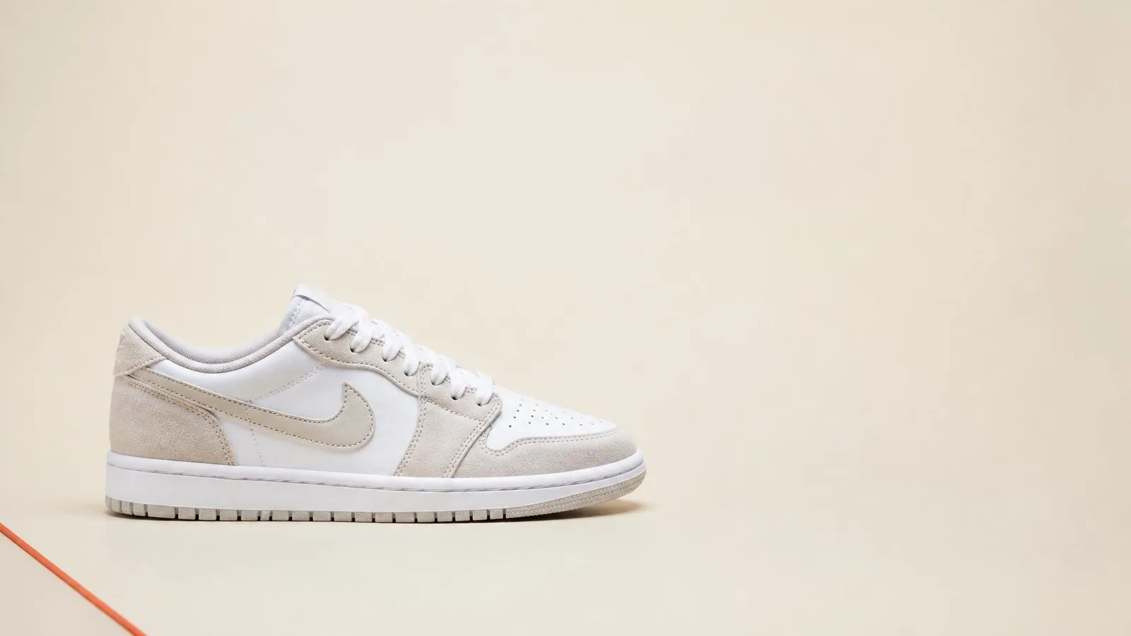 A single pair of clean, dead-stock sneakers shot in catalogue style against a warm cream background, centred left in the frame with open space for a title overlay.