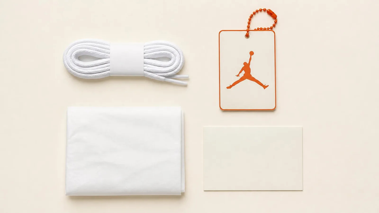 Flat-lay of sneaker accessories including coiled original laces, a hang tag, folded tissue paper, and a card insert arranged on an off-white surface.