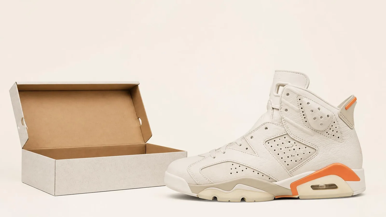 A high-top sneaker in side profile next to its open, empty original shoebox with no laces or tissue paper inside, shown against a warm off-white background.
