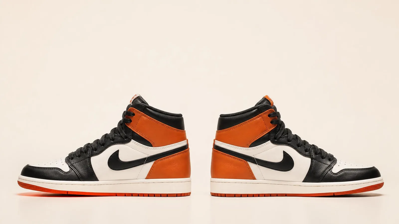 Two identical Jordan 1 high-top sneakers placed side by side in catalogue-style side profile on a white background, tongue tags subtly visible, illustrating how two authentic pairs of the same colorway can carry different country-of-origin labels.