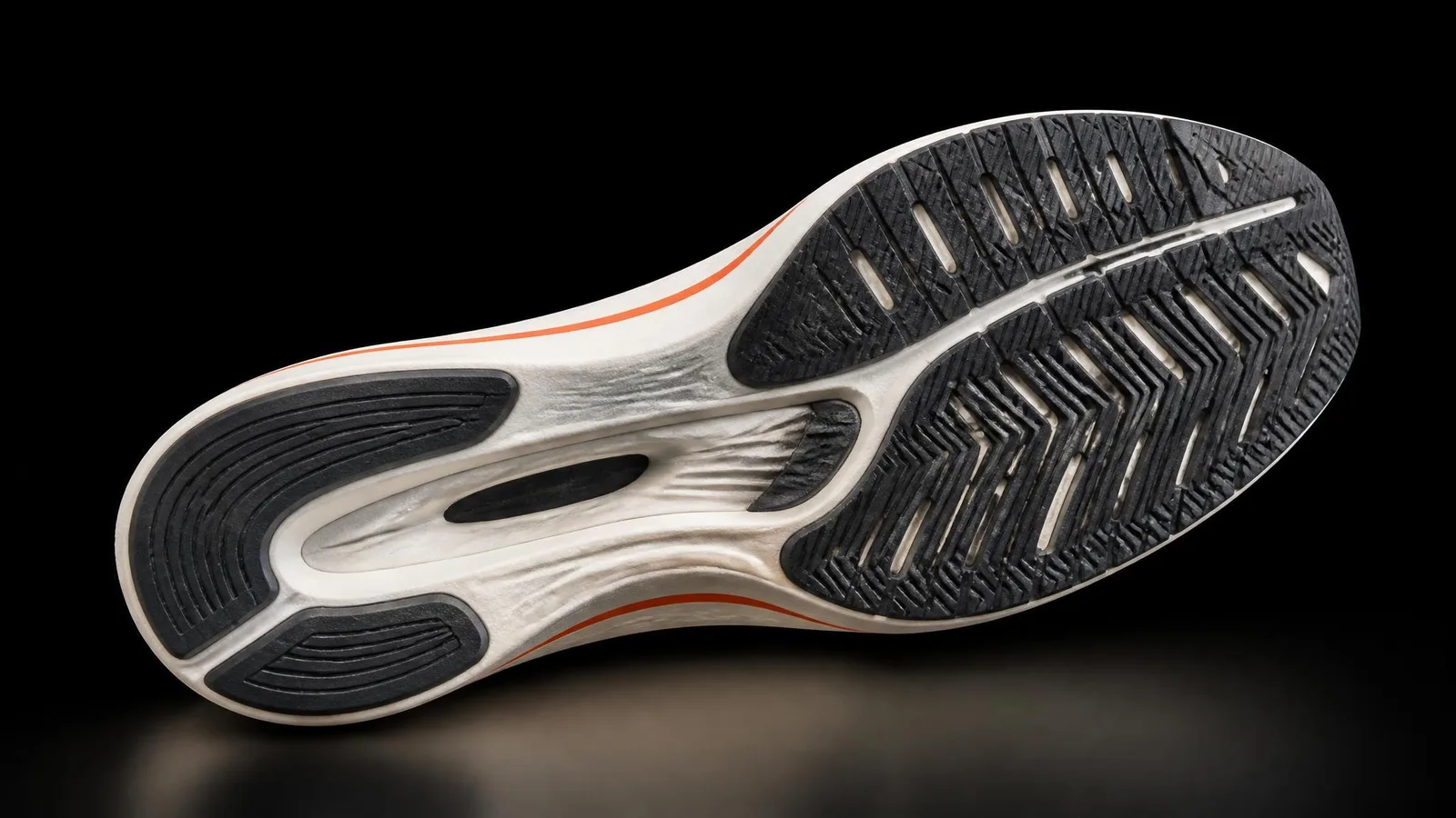 Close-up catalogue shot of a sneaker sole facing upward against a dark background, showing midsole and outsole construction detail with a warm orange accent stripe along the midsole edge.