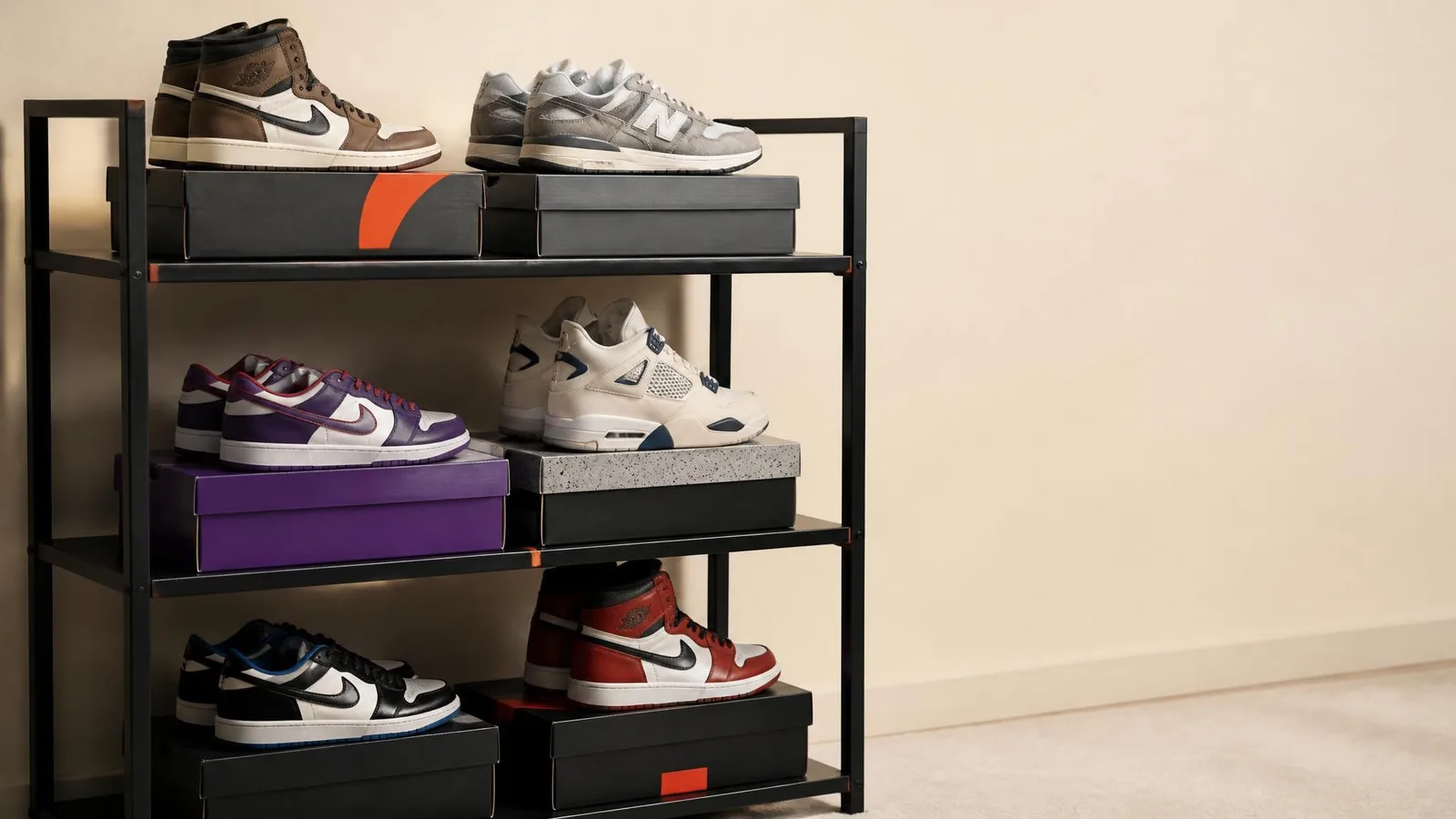 A neatly arranged collector's sneaker shelf holding several pairs of Jordans, Dunks, and New Balance sneakers in dead-stock condition, photographed in a clean three-quarter angle against a warm cream background.